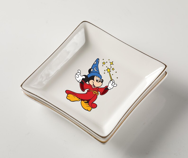 May include: Square white ceramic dish with gold trim featuring a colorful graphic of Mickey Mouse in a wizard costume. Mickey is holding a wand with stars. The dish is likely for decorative use or serving small items.