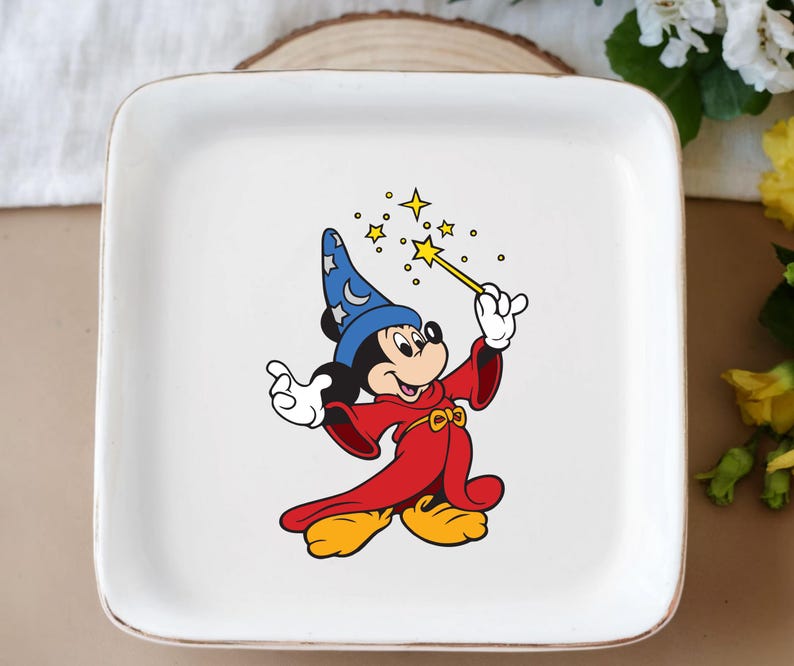 May include: White square ceramic plate featuring a cartoon image of Mickey Mouse dressed as a wizard. Mickey is wearing a blue hat with stars, a red robe, and yellow shoes, holding a wand with yellow stars.