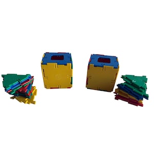 Puede incluir: Bloques de construcción coloridos en amarillo, azul, rojo y verde. Se ven dos estructuras cúbicas ensambladas, junto con pilas de piezas individuales. Los bloques están diseñados para entrelazarse, promoviendo la construcción y el juego creativos.
