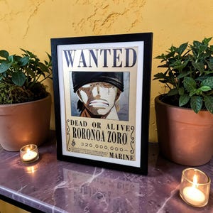 Può includere: Poster incorniciato "Wanted" con Roronoa Zoro di One Piece. Il poster ha una cornice nera e mostra un ritratto del personaggio con la scritta "WANTED" in alto e "DEAD OR ALIVE" in basso. Il poster è su una superficie di marmo.