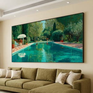 May include: A large framed painting of a swimming pool scene. The turquoise water reflects the surrounding greenery and blue sky. Red and white tiles border the pool, and a white umbrella and chairs are visible. The artwork is displayed above a green sofa in a living room.