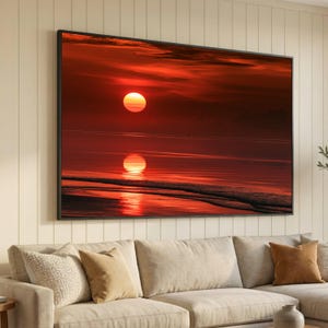May include: A rectangular wall art print featuring a vibrant sunset over a calm ocean. The sun is a bright orange sphere hanging low in a deep red sky, casting a glowing reflection across the dark water and the wet sand of the shoreline.