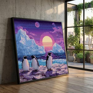 May include: Framed art print featuring three penguins standing on a rocky shore. The pixelated artwork depicts a sunset over the ocean with icebergs and a purple and orange sky. The print is in a black frame and leans against a concrete wall.