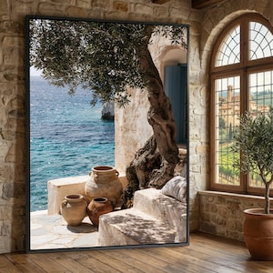 Può includere: Una grande stampa artistica da parete rettangolare incorniciata che raffigura una scena costiera mediterranea con un ulivo, tre vasi in terracotta su gradini di pietra e una vista sul mare blu. L'immagine è incorniciata da un sottile bordo nero.