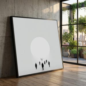 Puede incluir: Impresión artística enmarcada con un diseño minimalista. La obra representa siluetas de personas caminando hacia una fuente de luz circular y brillante. La impresión está sobre un fondo blanco, enmarcada en negro y apoyada contra una pared de hormigón.