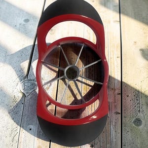 May include: A red and black apple slicer featuring a circular frame with eight sharp metal blades radiating from a central ring. The tool has two ergonomic handles on opposite sides, designed for pressing down to core and slice fruit evenly.