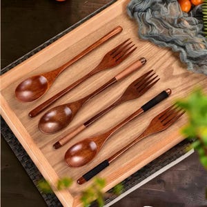 May include: A set of three long-handled wooden spoons and three matching wooden forks. The utensils feature a polished dark brown wood grain finish. Two of the forks and one spoon have contrasting black or tan wrapped handles at the ends.
