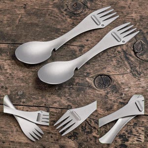May include: Two silver-coloured metal sporks featuring a spoon-shaped bowl at one end and a four-tined fork at the other. The fork end includes a serrated edge on one side and a small rectangular cutout. The design is matte and metallic.