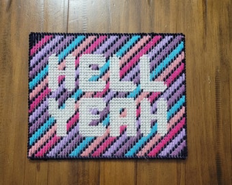 May include: A colorful cross-stitch piece with a striped background and the words "Hell Yeah" in white.