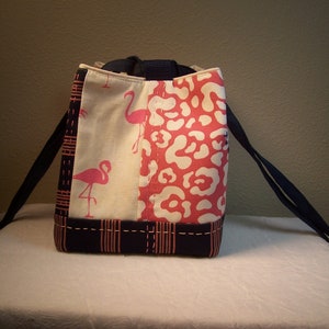 May include: A black and white tote bag with pink flamingo and leopard print fabric panels. The bag has black straps and a zipper closure.