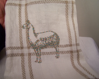 Puede incluir: Toalla de cocina blanca con un patrón de cuadros marrones y un diseño de llama bordado. La llama está bordada con cuentas verdes y doradas.