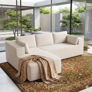 May include: A cream-colored sectional sofa with a striped pattern, featuring multiple cushions and an attached chaise lounge. A brown throw blanket with fringe rests on the chaise. The sofa sits on a patterned rug.