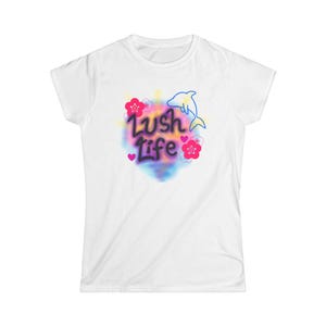 May include: White t-shirt with a colorful graphic. The design features the words "Lush Life" in a stylized font, a blue dolphin, pink flowers, and small pink hearts. The graphic has a watercolor effect.