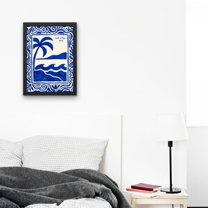 Könnte beinhalten: Gerahmter Kunstdruck mit einer blau-weißen Küstenlandschaft. Das Kunstwerk zeigt eine Palme, Wellen und eine Küstenlinie, mit dem Text "Cote d'Azur 1953". Der Druck ist in einem schwarzen Rahmen.