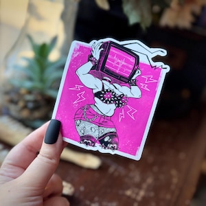 May include: A pink sticker featuring a muscular figure with a television for a head. The TV screen displays a heartbeat monitor. The figure wears a studded bra, shorts, and bracelets. Lightning bolt graphics surround the figure.