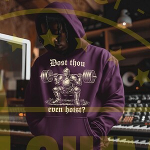 Puede incluir: Una sudadera con capucha de color p&uacute;rpura oscuro con un gr&aacute;fico de un caballero levantando una barra. El texto "Dost thou even hoist?" est&aacute; impreso debajo. La sudadera tiene una capucha con cord&oacute;n y un bolsillo delantero.
