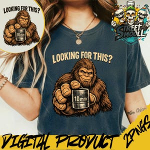 Puede incluir: Camiseta azul marino con un dibujo animado de Bigfoot sosteniendo un cilindro de 10 mm. El texto "LOOKING FOR THIS?" está encima de Bigfoot. La camiseta también tiene el texto "DIGITAL PRODUCT 2PNGS".
