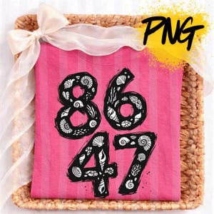 Puede incluir: Una camiseta rosa con rayas verticales, con los números 8647 en negro, cada número relleno con ilustraciones de conchas marinas. La camiseta se presenta sobre una bandeja tejida con un lazo de cinta transparente.