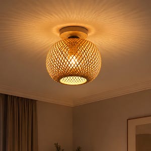 Peut inclure: Un plafonnier sphérique doté d'un abat-jour en treillis de bambou tressé de couleur beige naturel. La lampe est allumée, projetant une lueur chaude et des motifs d'ombres complexes et rayonnants sur la surface du plafond environnant.