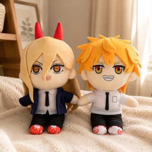 May include: Two plush dolls featuring anime-style characters. The left doll has long blonde hair, red horns, a dark blue jacket, white shirt, black tie, black pants, and red shoes. The right doll has spiky orange hair, a white shirt, black tie, black pants, and white shoes.