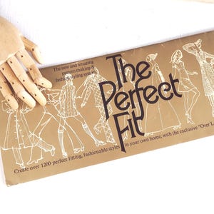 May include: A vintage sewing pattern guide titled "The Perfect Fit" in brown and white. The cover features illustrations of fashionable styles and text promoting a pattern-making system. The guide promises over 1200 fitting styles.