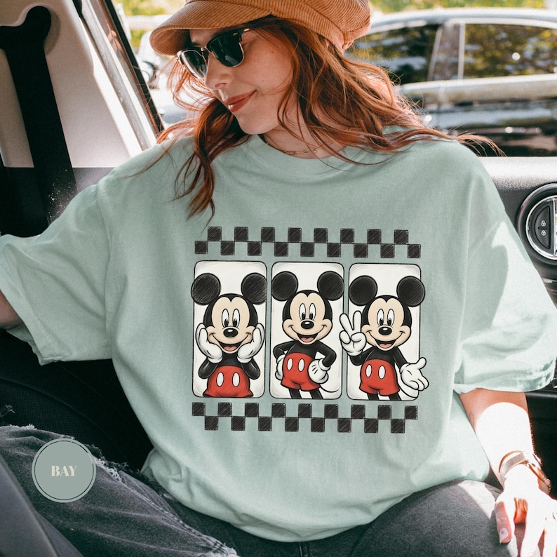 Puede incluir: Camiseta verde claro con tres im&aacute;genes de Mickey Mouse en marcos rectangulares con un borde a cuadros blanco y negro. Mickey se muestra en varias poses, con pantalones cortos rojos y guantes blancos.