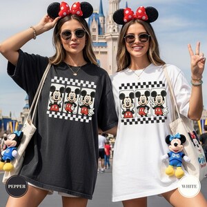 Puede incluir: Camisetas negras y blancas con un gr&aacute;fico de Mickey Mouse. El gr&aacute;fico muestra a Mickey en tres poses diferentes, sobre un fondo a cuadros. Las camisetas se usan con orejas de Mickey Mouse.