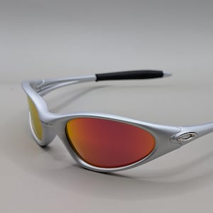 May include: Silver-framed sunglasses with red and yellow lenses. The sunglasses have a sleek, modern design with black accents on the temples. The lenses have a gradient effect, transitioning from red to yellow.