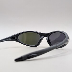 May include: Black sunglasses with oval lenses and a sleek, modern design. The sunglasses have a matte finish and curved temples for a comfortable fit. The lenses are tinted, providing protection from the sun. A stylish accessory for outdoor activities.