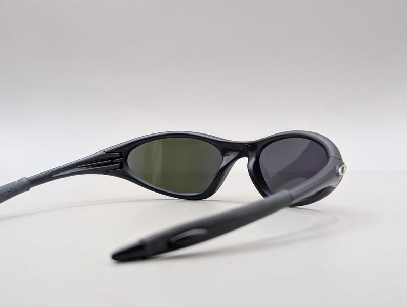 May include: Black sunglasses with oval lenses and a sleek, modern design. The sunglasses have a matte finish and curved temples for a comfortable fit. The lenses are tinted, providing protection from the sun. A stylish accessory for outdoor activities.