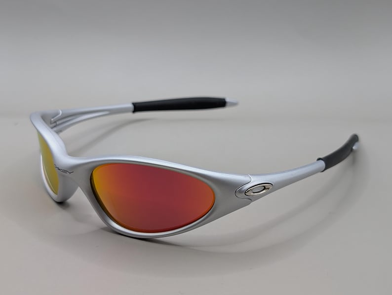 May include: Silver-framed sunglasses with red and yellow lenses. The sunglasses have a sleek, modern design with black accents on the temples. The lenses have a gradient effect, transitioning from red to yellow.