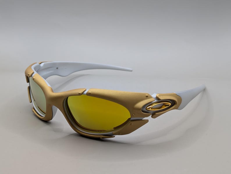 Pu&ograve; includere: Occhiali da sole dorati e bianchi con lenti gialle. Gli occhiali da sole hanno un design sportivo con montatura dorata e aste bianche. Le lenti sono di colore giallo brillante e lo stile generale &egrave; moderno ed elegante.