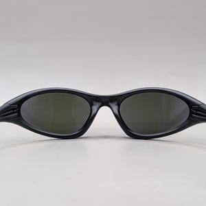 May include: Black sunglasses with a sleek, sporty design. The frames are matte black, and the lenses have a dark tint. The arms curve back for a secure fit. These sunglasses are suitable for outdoor activities.