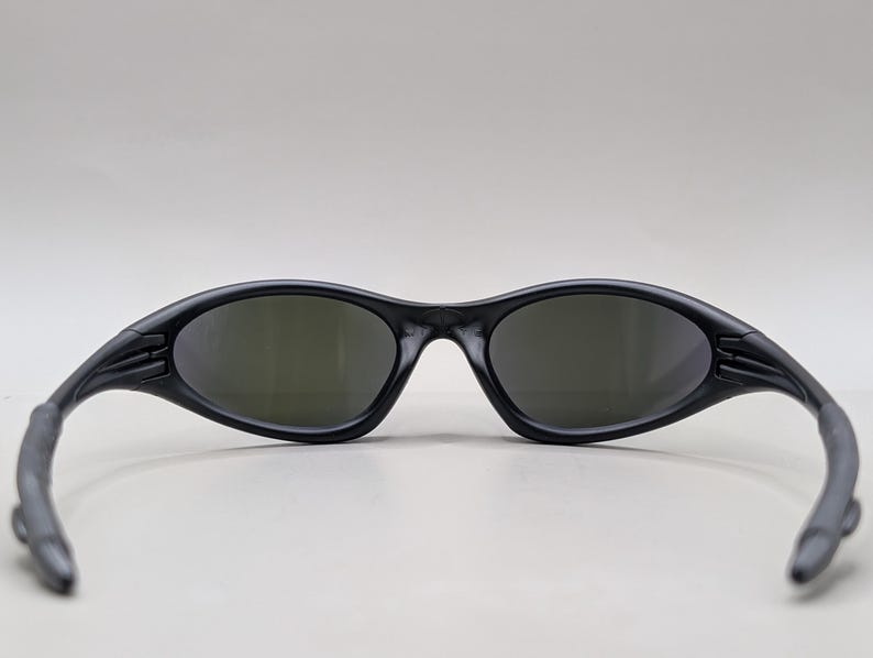 May include: Black sunglasses with a sleek, sporty design. The frames are matte black, and the lenses have a dark tint. The arms curve back for a secure fit. These sunglasses are suitable for outdoor activities.