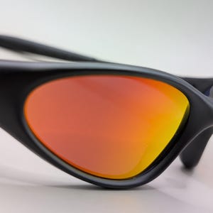 Pode incluir: &Oacute;culos de sol pretos com lentes degrad&ecirc; laranja e amarelo. Os &oacute;culos de sol t&ecirc;m um design elegante e moderno com acabamento fosco. As lentes s&atilde;o curvas e proporcionam um contraste vibrante com a arma&ccedil;&atilde;o preta.
