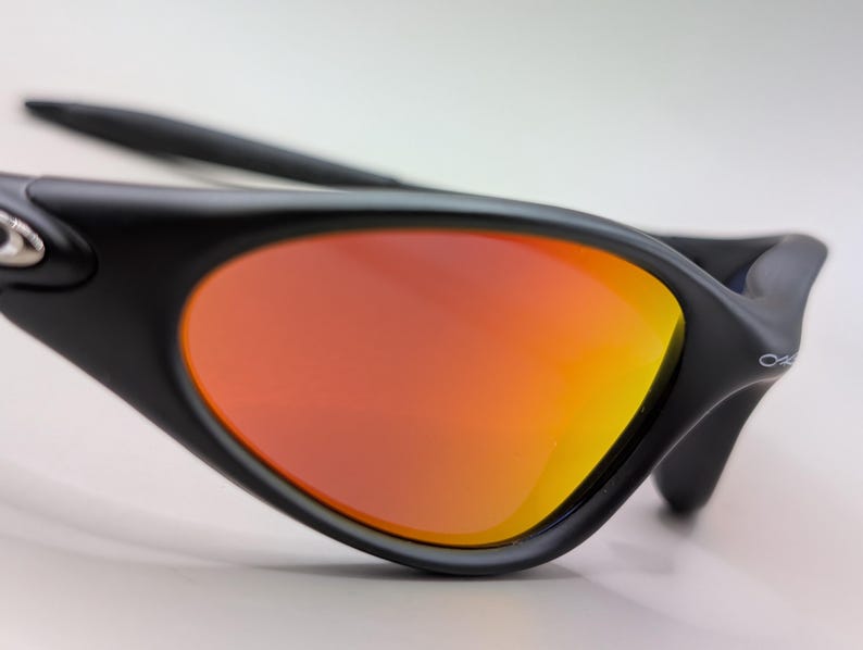 Pode incluir: &Oacute;culos de sol pretos com lentes degrad&ecirc; laranja e amarelo. Os &oacute;culos de sol t&ecirc;m um design elegante e moderno com acabamento fosco. As lentes s&atilde;o curvas e proporcionam um contraste vibrante com a arma&ccedil;&atilde;o preta.