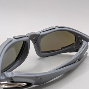 K&ouml;nnte beinhalten: Graue Sonnenbrille mit sportlichem Design. Die Brille hat einen umlaufenden Rahmen und get&ouml;nte Gl&auml;ser. Der Rahmen ist mattgrau, die Gl&auml;ser leicht braun get&ouml;nt. Sie ist f&uuml;r Outdoor-Aktivit&auml;ten konzipiert.