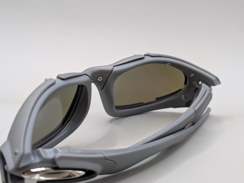 K&ouml;nnte beinhalten: Graue Sonnenbrille mit sportlichem Design. Die Brille hat einen umlaufenden Rahmen und get&ouml;nte Gl&auml;ser. Der Rahmen ist mattgrau, die Gl&auml;ser leicht braun get&ouml;nt. Sie ist f&uuml;r Outdoor-Aktivit&auml;ten konzipiert.