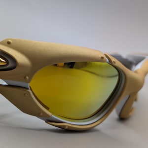 Pu&ograve; includere: Primo piano di occhiali da sole dorati e bianchi con lenti gialle. Gli occhiali da sole hanno un design moderno con montatura dorata e dettagli bianchi. Le lenti sono di colore giallo brillante.
