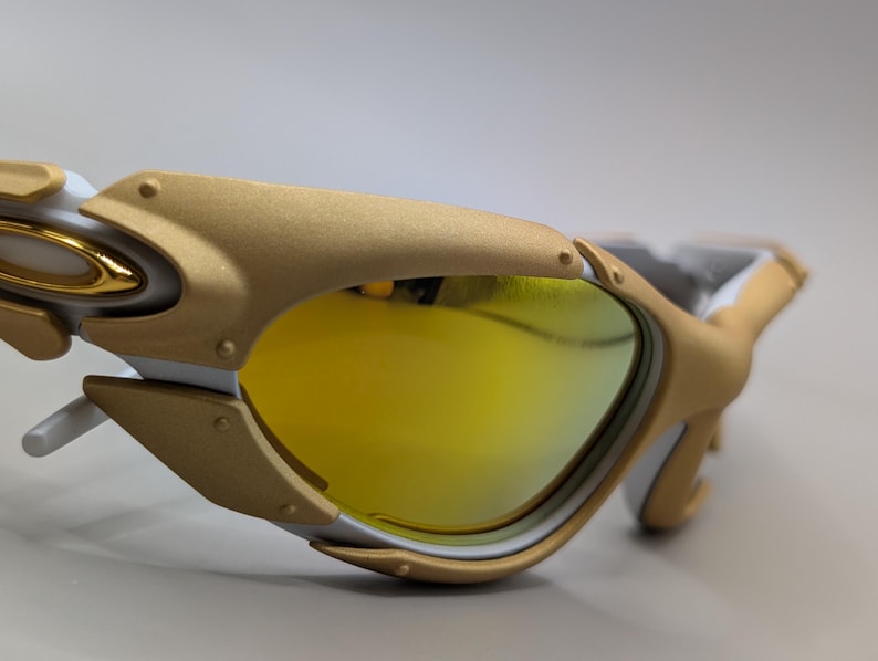 Pu&ograve; includere: Primo piano di occhiali da sole dorati e bianchi con lenti gialle. Gli occhiali da sole hanno un design moderno con montatura dorata e dettagli bianchi. Le lenti sono di colore giallo brillante.