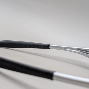 May include: Close-up of silver-framed sunglasses with black rubber grips. The text "MADE IN U.S.A." is visible on the temple arm. The lenses are a light blue color.