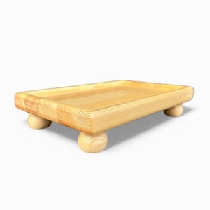 Könnte beinhalten: Ein rechteckiges Serviertablett aus Holz mit abgerundeten Ecken und einer flachen, vertieften Fläche. Das Tablett wird von vier kleinen, abgerundeten Füßen getragen. Das Holz hat eine helle, natürliche Farbe und sichtbare Maserung.
