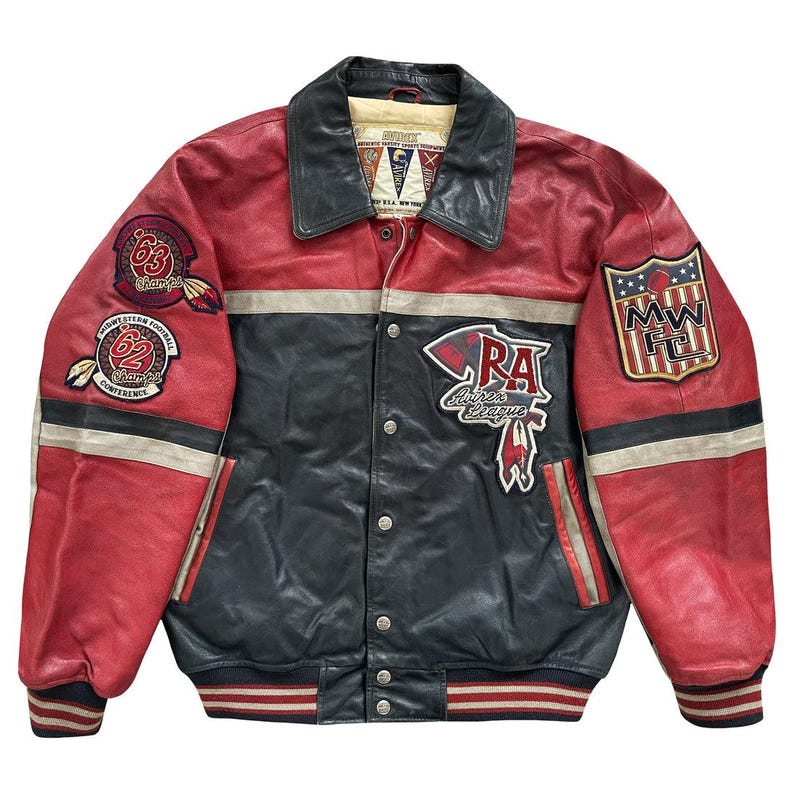 Peut inclure: Veste en cuir vintage rouge, noir et gris, orn&eacute;e de nombreux &eacute;cussons. La veste a une fermeture boutonn&eacute;e, un col noir et des poignets ray&eacute;s. Les &eacute;cussons incluent "63 Champs", "62 Conference" et "RA Aires League".