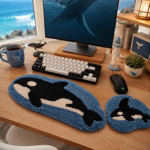 May include: A tufted textile set featuring a long rectangular keyboard mat and a smaller circular mouse pad, both in a blue background with a black and white orca whale design. The textured surface displays a detailed depiction of the marine mammal.