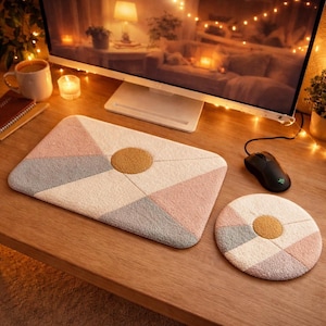 Può includere: Un set di tappetino da scrivania e sottobicchiere geometrici. Il tappetino è un rettangolo con un cerchio centrale, con sezioni rosa, grigie e crema. Il sottobicchiere rispecchia il design. Entrambi hanno un cerchio marrone al centro.