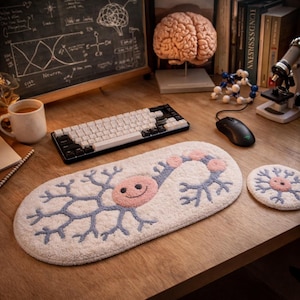 Może przedstawiać: Biała, owalna mata na biurko i pasujący podkładka pod kubek z uśmiechniętym różowym wzorem neuronu z niebieskimi i różowymi akcentami. Czarno-biała klawiatura i mysz komputerowa również znajdują się na drewnianym biurku.