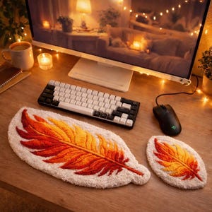 May include: A desk arrangement with a white and black mechanical keyboard, a black mouse, and two feather-shaped rugs. The rugs have orange and yellow gradients on a white base. The desk is made of wood.