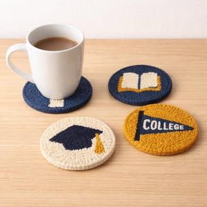 Puede incluir: Cuatro posavasos redondos cosidos a mano con diseños universitarios. Un posavasos tiene un birrete, otro un libro abierto y un tercero una bandera que dice "COLLEGE". Una taza blanca con café se encuentra sobre un posavasos azul.