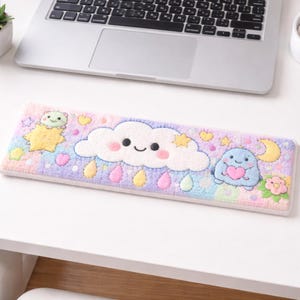 May include: A rectangular, pastel-colored mousepad featuring a smiling cloud, raindrops, stars, and cartoon characters. The mousepad is designed with a soft, plush texture and is placed on a white desk near a laptop.