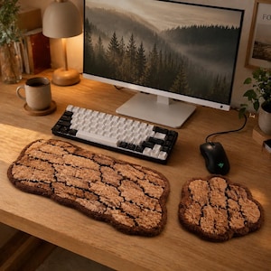 May include: A wooden desk setup featuring a keyboard, mouse, and a matching brown, textured mousepad and wrist rest. A computer monitor displays a forest scene. A mug and lamp are also on the desk.